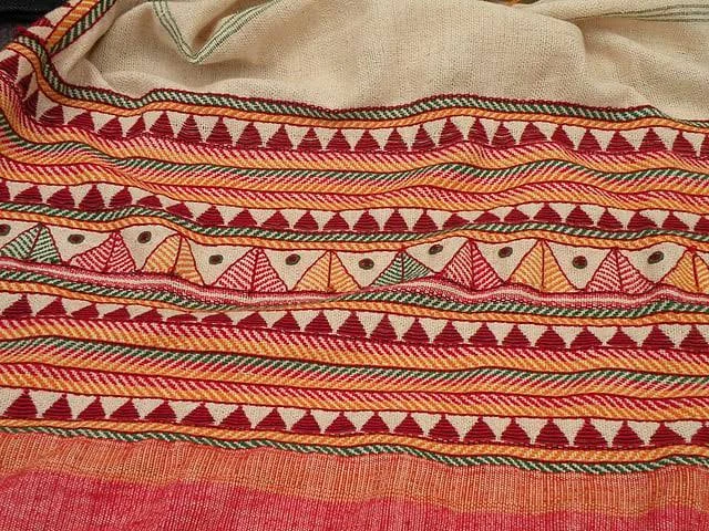 Close-up of a Dongria Kondh kapdaganda shawl — bands of red, orange and green triangles hand-embroidered on coarse cream cotton